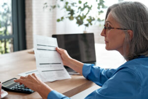 An older woman holding a piece of paper while using a calculator.