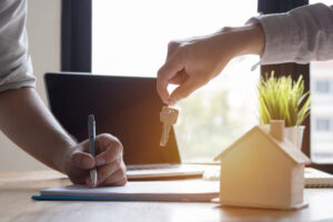 A man signing paperwork as someone holds out a house key.