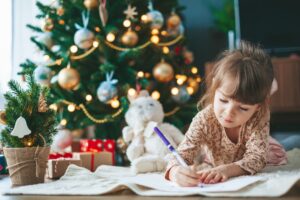 A girl writing a letter in front of a Christmas tree.